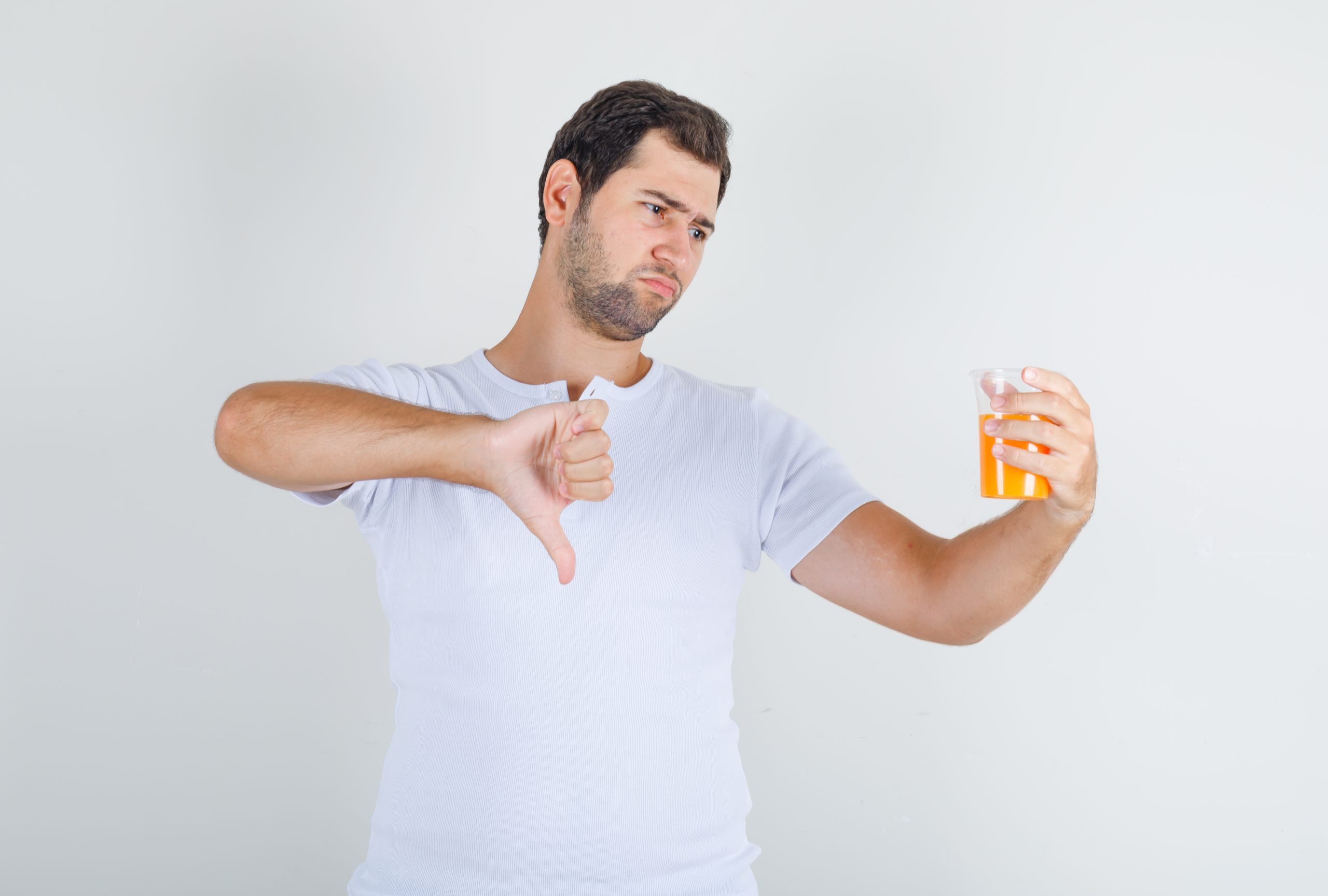 Young male showing thumb down with juice in white t-shirt and looking dissatisfied. front view.